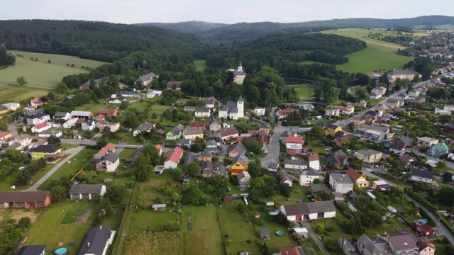 Letecký pohled na celou Raduň se zámkem, kostelem a okolními lesnatými kopci.
