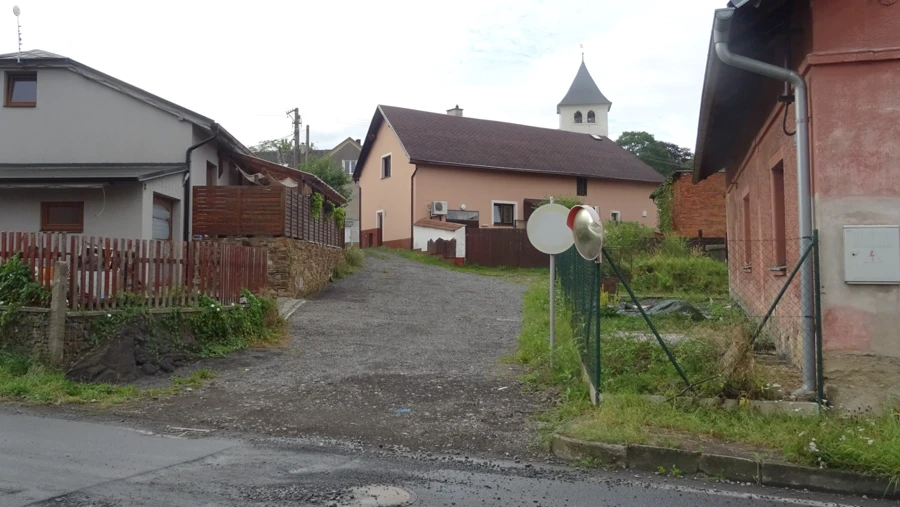 Ulička Příčná v Raduni dnes — nezpevněný povrch, vyrůstající zeleň a chybějící dopravní značky