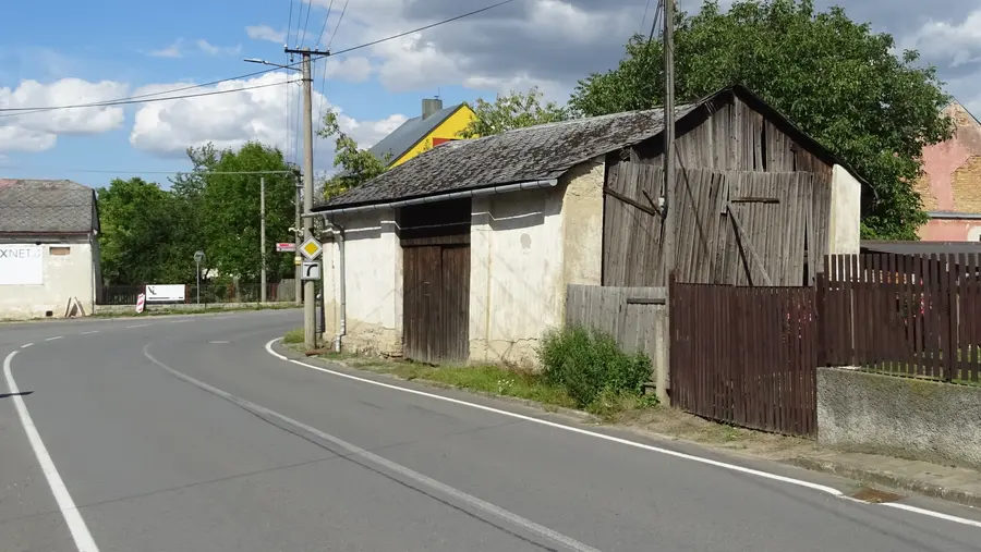 Zarostlý chodník u hlavní silnice v centru Raduně — na místě chodníku rostou kopřivy