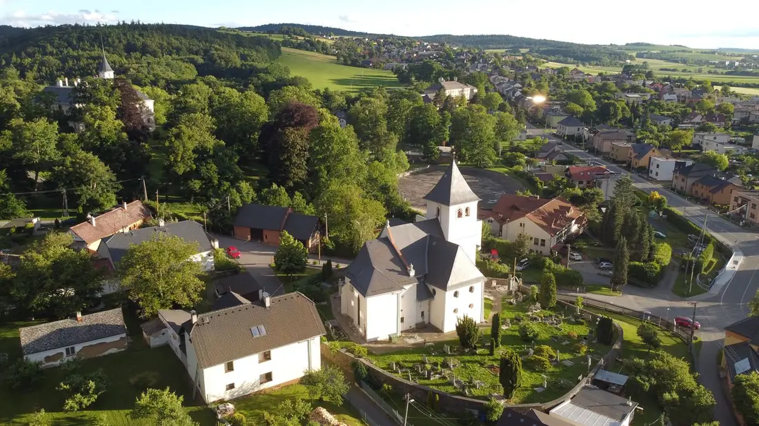 Letecký pohled shora na kostel Nejsvětější Trojice obklopený zástavbou rodinných domů.