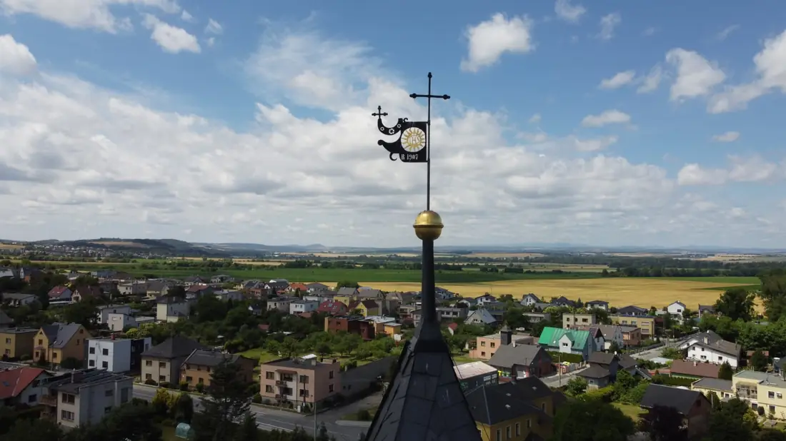 Detail větrné korouhve s křížem a letopočtem 1907 na vrcholu věže s výhledem na Raduň.